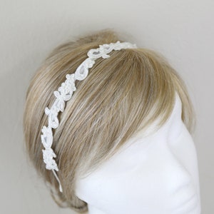 May include: A white lace headband with floral and teardrop-shaped details. The delicate design is set against a light background, showcasing the intricate patterns. This elegant accessory is perfect for special occasions.