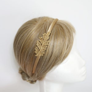 May include: A gold headband with a delicate gold leaf design. The headband is made of satin and is perfect for adding a touch of elegance to any outfit.