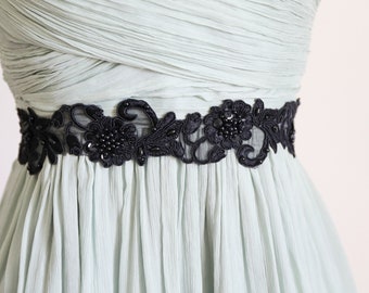 May include: A light blue dress with a black floral embroidered belt. The belt features intricate floral designs with beaded accents. The dress has a pleated bodice and skirt, creating a flowing silhouette. The overall aesthetic is elegant and suitable for formal occasions.