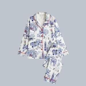 Può includere: Set pigiama bianco con stampa di paesaggio urbano blu e rosso. La parte superiore a maniche lunghe e i pantaloni presentano monumenti iconici e finiture rosse. Il set include una camicia con bottoni e pantaloni abbinati.