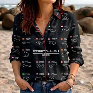 Könnte beinhalten: Ein schwarzes, langärmeliges Hemd mit Knopfleiste und einem weißen Formula 1 2026 Grafikdruck. Das Design zeigt verschiedene Rennstrecken-Umrisse, Nationalflaggen, Städtenamen und Daten. Das Hemd hat einen roten Saum am Kragen und an der Knopfleiste.