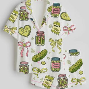 Puede incluir: Un conjunto de pijama blanco de manga corta con camisa abotonada y pantalón corto, con un estampado repetitivo de tarros de pepinillos con la etiqueta Classic Crunch, bolsas de snacks, pepinillos en forma de corazón y lazos amarillos.