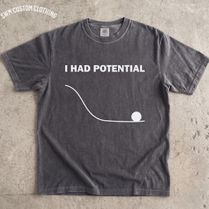 Könnte beinhalten: Ein anthrazitfarbenes Kurzarm-T-Shirt mit dem weißen Text I HAD POTENTIAL und einer Grafik eines weißen Balls, der am unteren Ende einer geschwungenen Linie liegt. Das Shirt hat einen Rundhalsausschnitt und eine verwaschene Optik.