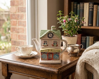 May include: A white ceramic mug with a black handle and the text "But First, Coffee" in a bold, black font. The mug is set against a blurred background, suggesting a cosy setting.