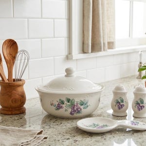 May include: A white ceramic mug with a black handle and the text "But First, Coffee" in a black, bold font. The mug is on a white surface.