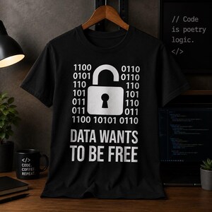 Op de afbeelding: Zwart t-shirt met een witte afbeelding van een hangslot en binaire code. De tekst "DATA WANTS TO BE FREE" staat eronder. Een koffiemok met "CODE. COFFEE. REPEAT" is zichtbaar.