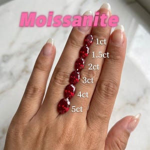 May include: Six oval-cut red Moissanite gemstones arranged in a vertical line, labeled with weights from 1ct to 5ct. The stones exhibit a deep crimson hue and faceted surfaces, showcasing a graduated size progression from the smallest to largest.