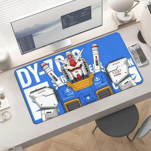 K&ouml;nnte beinhalten: Blauer rechteckiger Schreibtischunterlage mit einer Roboterillustration. Der Roboter ist &uuml;berwiegend blau, wei&szlig;, rot und gelb. Der Text "DY-700" ist auf der linken Seite der Unterlage aufgedruckt. Die Unterlage liegt auf einem wei&szlig;en Schreibtisch. Die Unterlage ist ca. 80 cm lang.