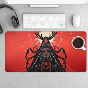 May include: A red and black desk mat featuring a stylized illustration of a hooded figure with insect-like features. The design includes a spider, a skull, and a web pattern. A white keyboard, mouse, and coffee cup are visible.