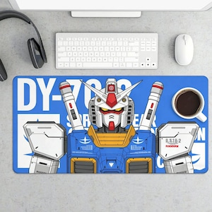 K&ouml;nnte beinhalten: Blaues rechteckiges Schreibtisch-Pad mit einer detaillierten Illustration eines Gundam-Roboters. Der Roboter ist haupts&auml;chlich blau, wei&szlig;, rot und gelb, mit dem Text "DY-782" und japanischem Text. Eine Tasse Kaffee und Computerzubeh&ouml;r sind sichtbar.