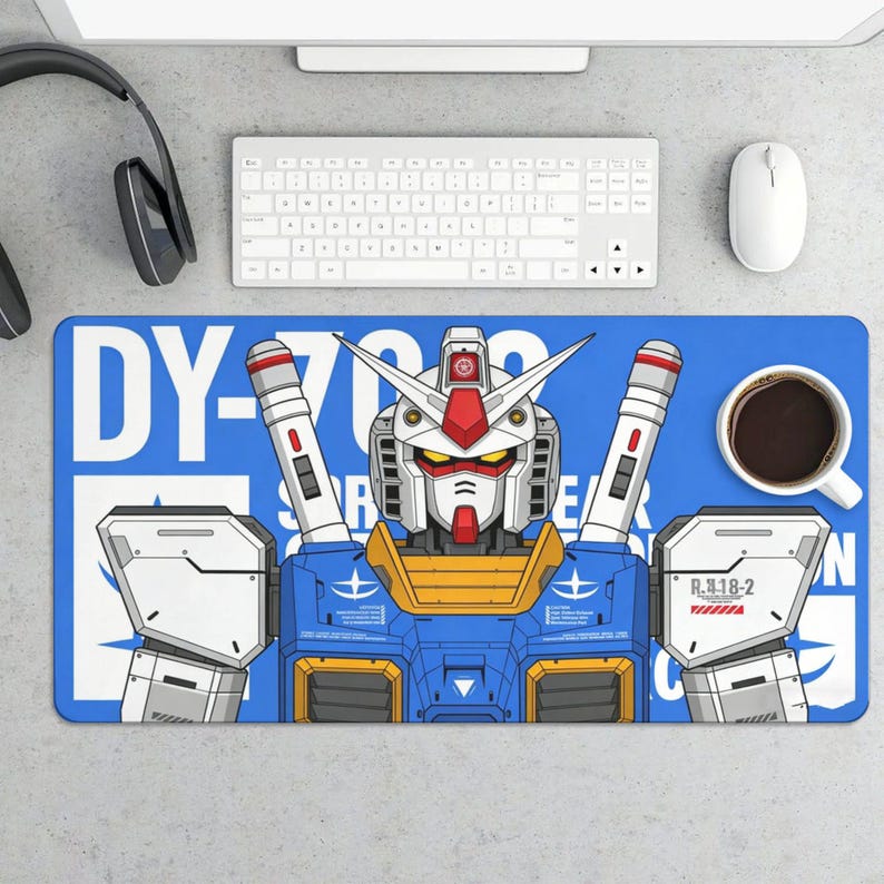 K&ouml;nnte beinhalten: Blaues rechteckiges Schreibtisch-Pad mit einer detaillierten Illustration eines Gundam-Roboters. Der Roboter ist haupts&auml;chlich blau, wei&szlig;, rot und gelb, mit dem Text "DY-782" und japanischem Text. Eine Tasse Kaffee und Computerzubeh&ouml;r sind sichtbar.