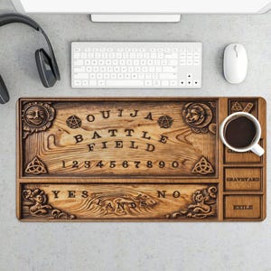May include: A wooden Ouija board desk mat with a coffee cup, keyboard, and mouse. The board features carved letters, numbers, and symbols, including a sun, pentagrams, and a lion's head. The words "OUJIA BATTLE FIELD" are prominently displayed.