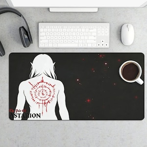 May include: Black rectangular mousepad featuring a white illustration of a figure with long hair and a red tattoo on the back. The text "The Pale Elf Astarion" is printed on the bottom left. A cup of coffee sits on the right.