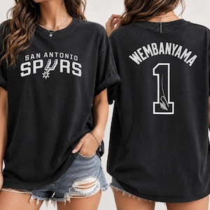 Pu&ograve; includere: Una t-shirt nera a maniche corte con il logo e la scritta San Antonio Spurs sul davanti. Il retro della maglietta mostra il nome Wembanyama in un arco sopra il numero 1, che include una grafica con firma in lettere bianche.