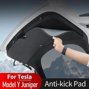May include: Black anti-kick pad for a Tesla Model Y Juniper. The pad is being installed in the trunk area of the car. The pad has a gray fabric interior and a black exterior. The text "For Tesla Model Y Juniper Anti-kick Pad" is visible.