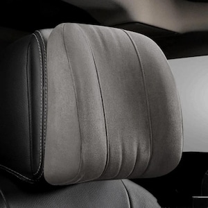 May include: A close-up of a car headrest. The headrest is gray and has a suede-like texture. The headrest is divided into three vertical sections with stitched seams. The sides of the headrest are black leather with white stitching.