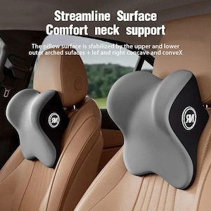 May include: Two gray and black car seat headrest pillows. The pillows have a curved design for neck support. The text "Streamline Surface Comfort neck support" is visible. Each pillow has a black section with a white logo.