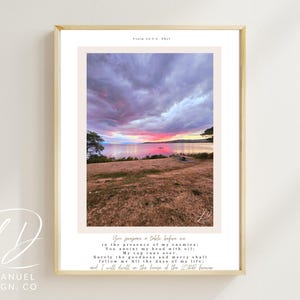 May include: A framed art print displaying a sunset over water, with a sky of pink and purple. The print includes a quote from Psalm 23:5 and the words "IMMANUEL DESIGN. CO" at the bottom, presented in a neutral colour palette.