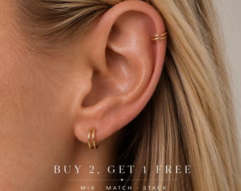 May include: A pair of gold-toned hoop earrings, one worn in the earlobe and one as a cartilage cuff. The text reads: BUY 2, GET 1 FREE. MIX · MATCH · STACK. The jewelry features a thin, circular design with a polished metallic finish.