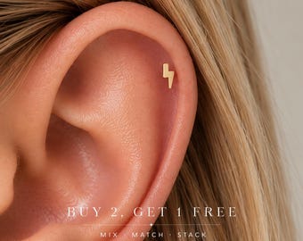 May include: A small gold-colored lightning bolt stud earring worn in the upper cartilage of an ear. The image includes the text: BUY 2, GET 1 FREE, MIX · MATCH · STACK. The earring features a simple, flat, geometric lightning bolt shape.