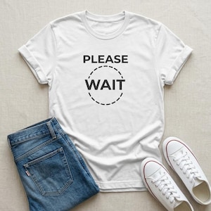 May include: A white short-sleeved t-shirt featuring the black text PLEASE WAIT enclosed within a dashed circular outline, paired with blue denim jeans and a pair of white canvas sneakers with red and blue trim along the rubber soles.