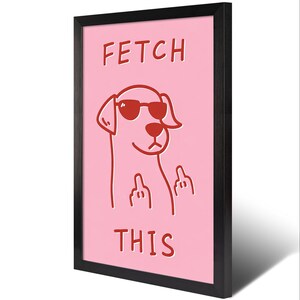 May include: A framed art print featuring a pink background with a red cartoon dog wearing sunglasses and giving the middle finger. The words "FETCH THIS" are printed in red above and below the dog illustration. The frame is black.