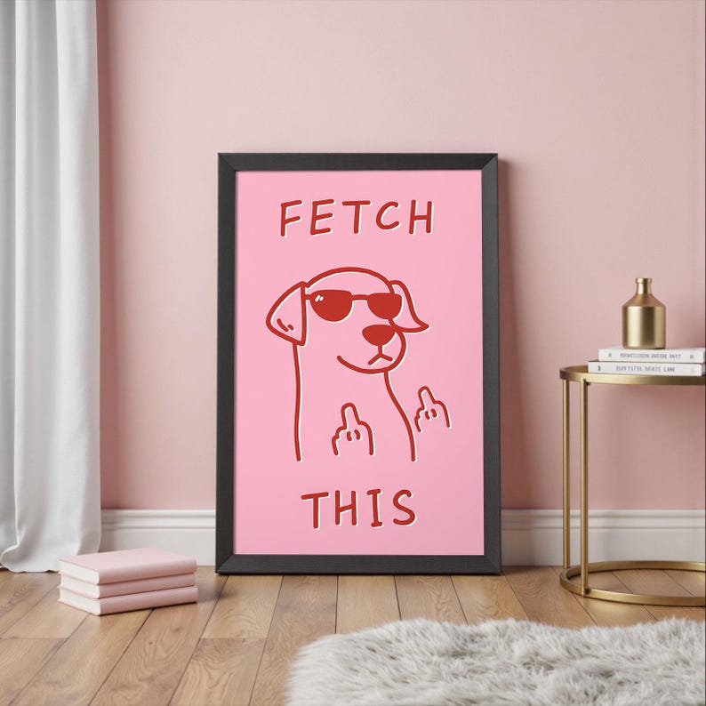 May include: Framed pink art print featuring a cartoon dog wearing sunglasses and giving the middle finger. The words "FETCH THIS" are printed in red above and below the dog illustration. The frame is black.