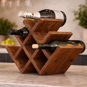 Puede incluir: Un botellero de madera oscura con un diseño en forma de diamante, que contiene tres botellas de vino. El botellero está hecho de madera marrón oscura y se encuentra sobre una encimera. Las botellas son de varios colores, incluyendo negro y verde.