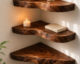 May include: Three tiered corner shelves made from dark brown natural wood with live edges. The top shelf holds a small amber glass vase with green foliage and a white candle. The middle shelf holds a white candle and a closed beige book.
