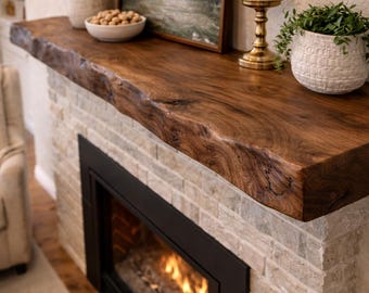 May include: A fireplace with a dark wood mantel and a brick facade. The mantel holds a framed landscape painting, a white candle in a gold holder, and a potted plant. A vase with dried plants and a bowl of nuts are also on the mantel.