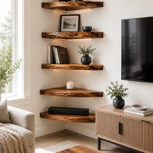 K&ouml;nnte beinhalten: F&uuml;nf gestufte Eckregale aus dunkelbraunem Holz mit nat&uuml;rlicher Baumkante. Jedes Regal verf&uuml;gt &uuml;ber eine integrierte, warmwei&szlig;e LED-Beleuchtung an der Unterseite. Die Regale sind in einer Ecke montiert und mit Pflanzen, B&uuml;chern und Kerzen best&uuml;ckt.