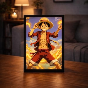 Könnte beinhalten: Gerahmter Anime-Kunstdruck mit einer Figur in roter Kleidung und Strohhut vor einem feurigen Hintergrund. Die Figur wird mit muskulösem Körperbau dargestellt, der seinen Hut hält. Das Kunstwerk wird auf einem Holztisch präsentiert.