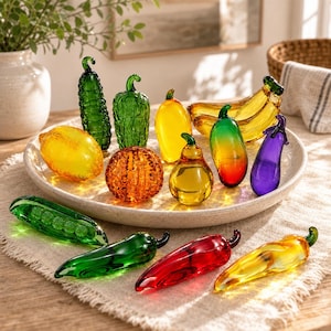 May include: A collection of colorful glass fruit and vegetable figurines including a green cucumber, a textured orange pumpkin, a yellow lemon, a red chili pepper, a purple eggplant, a green pea pod, and a yellow banana on a round plate.