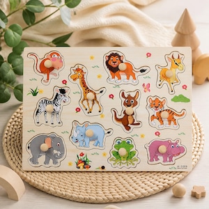 Puede incluir: Un rompecabezas de madera rectangular con piezas de agarre que muestra ilustraciones coloridas de un mono, jirafa, león, antílope, cebra, canguro, tigre, elefante, rinoceronte, rana e hipopótamo. Cada pieza tiene un pequeño pomo de madera.