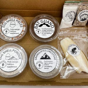 May include: A cardboard box containing four clear plastic containers filled with egg shell pieces, bat guano, egg shell powder, and granulated limestone, plus three clear plastic bags containing calcium powder, oyster shell, and a cuttlefish bone.