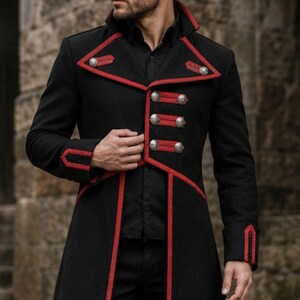 Peut inclure: Long manteau noir avec des bordures et des détails rouges. Le manteau présente un col haut, des boutons décoratifs et un passepoil rouge le long des bords. Le manteau est porté sur une chemise et un pantalon noirs.