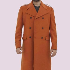 May include: A long, double-breasted orange coat with black buttons and two front pockets. The coat has a classic design with a notched lapel and shoulder straps. The coat is made of a wool-like material.