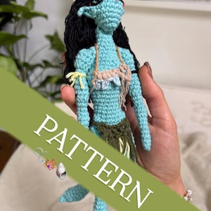 May include: A crocheted doll with a teal body, black hair, and a small bikini top. The doll has a green skirt and a tail. The word "PATTERN" is printed on a green banner across the image.