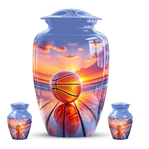 May include: A large cremation urn and two smaller matching keepsake urns featuring a glossy finish. The surface displays a vibrant sunset scene on a basketball court with a basketball in the centre, reflecting on the polished wooden floor.