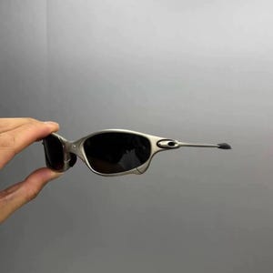 May include: Silver-framed sunglasses with dark lenses. The sunglasses have a sleek, modern design with a curved frame and extended temples. The lenses are dark, providing shade and protection from the sun.