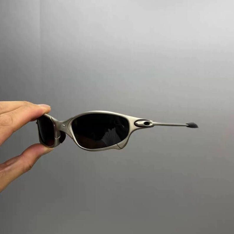 May include: Silver-framed sunglasses with dark lenses. The sunglasses have a sleek, modern design with a curved frame and extended temples. The lenses are dark, providing shade and protection from the sun.