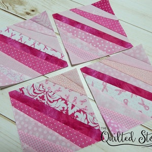 Könnte beinhalten: Vier rosa und weiße Stoffquadrate mit diagonalen Streifen. Die Stoffquadrate bestehen aus verschiedenen rosa und weißen gemusterten Stoffen, darunter rosa Schleifendesigns. Die Quadrate sind in einem Gittermuster auf einer weißen Holzoberfläche angeordnet. Der Text "The Quilted Story" ist in der unteren rechten Ecke des Bildes sichtbar.