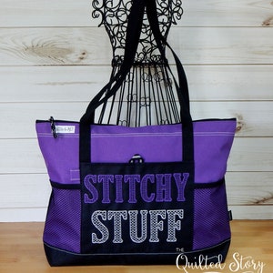 May include: A purple tote bag with black accents and handles. The front pocket features the embroidered text "STITCHY STUFF" in purple and white. The bag has mesh side pockets and a zipper closure. The words "The Quilted Story" are at the bottom.