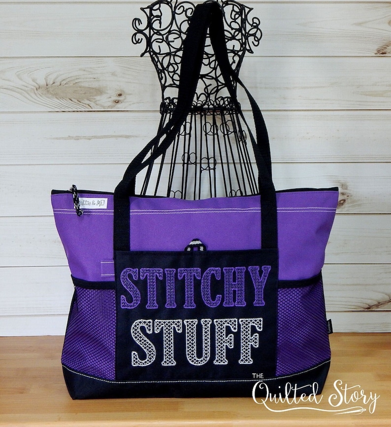 May include: A purple tote bag with black accents and handles. The front pocket features the words "Stitchy Stuff" in embroidered lettering. The bag has mesh side pockets and a zipper closure.
