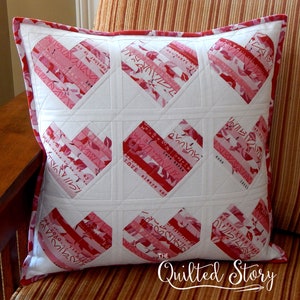 Puede incluir: Una almohada blanca con un patrón de corazones rojos y rosas. Los corazones están hechos de tiras de tela con las palabras "Love always and" y "Love birds" impresas en ellos. La almohada está acolchada con un patrón de diamante. El texto "The Quilted Story" está impreso en la parte inferior de la almohada.