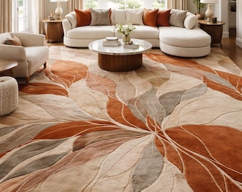 May include: A large area rug featuring a sweeping, organic leaf-like pattern in shades of burnt orange, beige, cream, and muted gray. The design consists of curved, flowing lines that create a sense of movement across the rectangular floor covering.