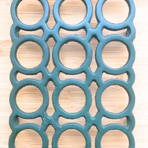 以下が含まれることがあります： 円形の開口部を備えた、濃い緑色の長方形の飲料缶キャリア。 キャリアは耐久性のある素材でできており、複数の缶を保持するように設計されています。 背景は明るい色の木材の表面です。