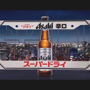 May include: A bottle of Asahi Super Dry beer with a silver label, set against a cityscape at night. The bottle is in front of a white rectangular frame with Japanese text and the words "SUPER DRY".