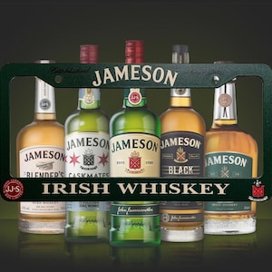 Può includere: Un assortimento di bottiglie di Jameson Irish Whiskey, presentate all'interno di una cornice verde per targa. La cornice riporta la scritta "JAMESON" e "IRISH WHISKEY". Le bottiglie hanno etichette e design diversi.