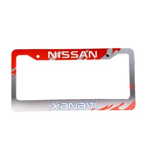 Könnte beinhalten: Ein rechteckiger Kennzeichenrahmen mit rotem und silbernem Design. Das Wort "NISSAN" steht oben in Rot und "xanaví" unten in Silber. Der Rahmen hat einen silbernen Rand mit roten flammenartigen Akzenten.